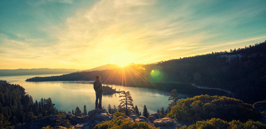 Man standing on rock looking out at lake and mountain view in the distance.